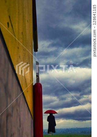 一位女士撐著一把紅傘,天空多雲 一位女士撐著一把紅傘,天空多雲 128641185