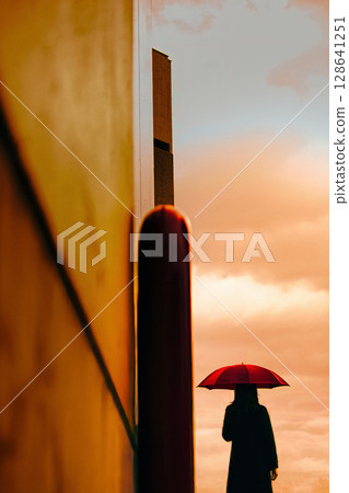 夕陽下撐著紅傘行走的女人 128641251