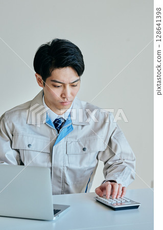 A young man in his twenties doing calculations on a calculator 128641398