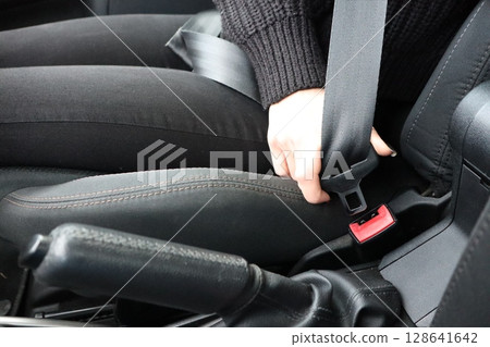 A woman is buckling her seatbelt in her car to ensure her safety during the journey 128641642