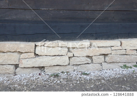 A rustic stone wall base stands proudly against a charming wooden structure nearby A rustic stone wall base stands proudly against a charming wooden structure nearby 128641888
