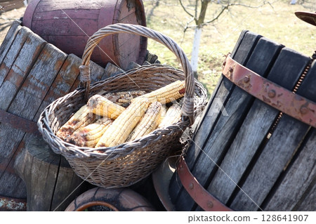 A Rustic BasketFilled with Dried Corn alongside Wooden Barrels for a countrythemed decor 128641907