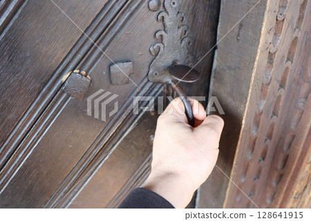 A hand gently reaching out for an intricately designed ornate door handle on a beautiful entrance A hand gently reaching out for an intricately designed ornate door handle on a beautiful entrance 128641915