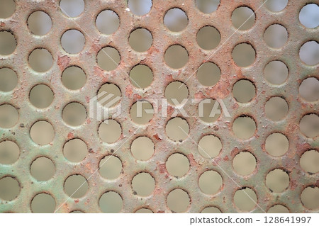 A closeup of a rusty, perforated metal surface evokes industrial heritage and age 128641997