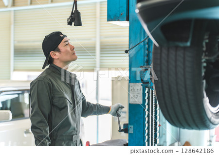A male mechanic lifting up a vehicle at a repair shop A male mechanic lifting up a vehicle at a repair shop 128642186