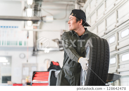 一名汽車修理工/機械師的中年亞洲男子拿著輪胎打招呼。 128642478