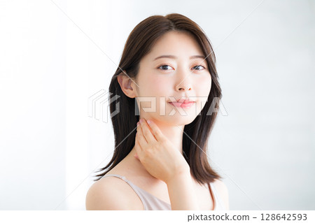 Beautiful young woman with beautiful bare skin poses touching her chin and neck, beauty and beauty image, looking at camera 128642593