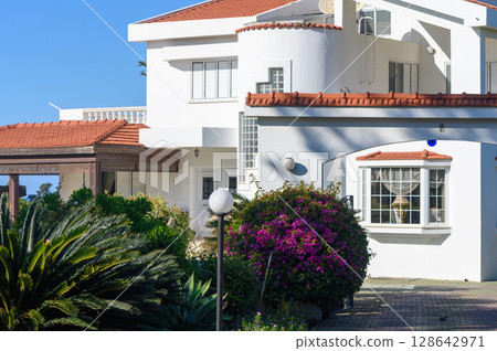 Charming villa surrounded by vibrant flowers in a sunny coastal location. Charming villa surrounded by vibrant flowers in a sunny coastal location. 128642971