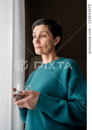Exhausted woman with water medicine by window in stillness alone. Emotional tress, quiet reflection 128643078