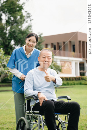 Elderly asian senior woman on wheelchair with Asian careful caregiver and encourage patient, walking in garden. with care from a caregiver Elderly asian senior woman on wheelchair with Asian careful caregiver and encourage patient, walking in garden. with care from a caregiver 128643968