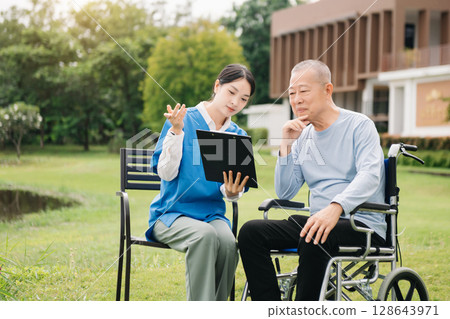 Asian careful caregiver or nurse and the happy patient in a wheelchair are walking in the garden. to help and encourage and rest your mind with green nature. Use a stethoscope to listen Asian careful caregiver or nurse and the happy patient in a wheelchair are walking in the garden. to help and encourage and rest your mind with green nature. Use a stethoscope to listen 128643971