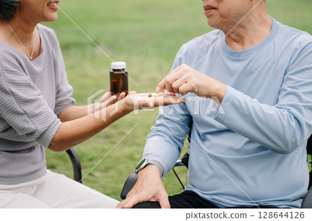 Asian Senior couple sitting in wheelchairs taking care of each other.in romantic time They laughing and smiling while sitting outdoor in park. 128644126