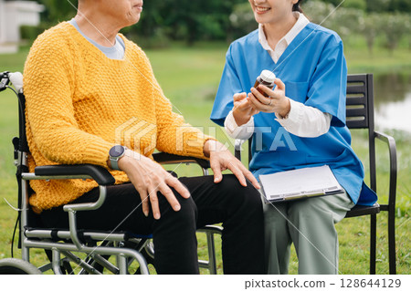 Asian careful caregiver or nurse and the happy patient in a wheelchair are walking in the garden. to help and encourage and rest your mind with green nature. Use a stethoscope to listen Asian careful caregiver or nurse and the happy patient in a wheelchair are walking in the garden. to help and encourage and rest your mind with green nature. Use a stethoscope to listen 128644129