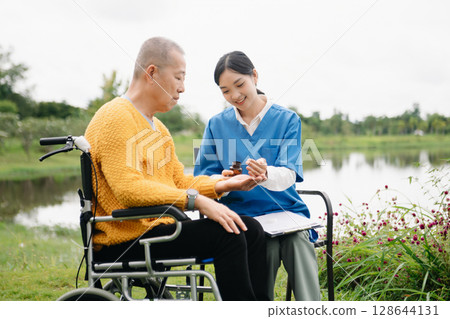 Asian young caregiver nurse support senior older male walking outdoors. Specialis doctor help and take care of elderly mature. Nursing home hospital garden 128644131