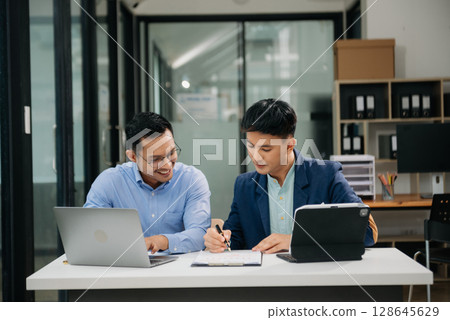 Two Asian businessman discuss investment project working and planning strategy with tablet laptop computer in modern office. Two Asian businessman discuss investment project working and planning strategy with tablet laptop computer in modern office. 128645629
