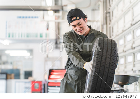 Male mechanic carrying tires at an auto repair shop (physical labor, heavy work, heavy, back pain) 128645978