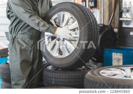 Male mechanic carrying tires at an auto repair shop (physical labor, heavy work, heavy, back pain) Male mechanic carrying tires at an auto repair shop (physical labor, heavy work, heavy, back pain) 128645983