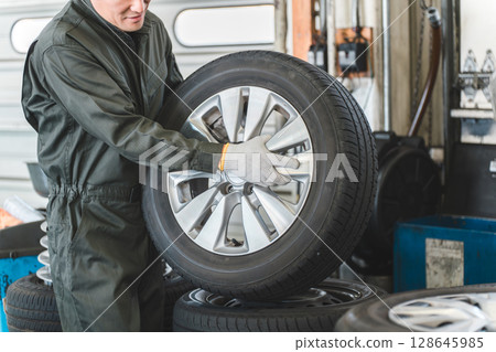 Male mechanic carrying tires at an auto repair shop (physical labor, heavy work, heavy, back pain) 128645985