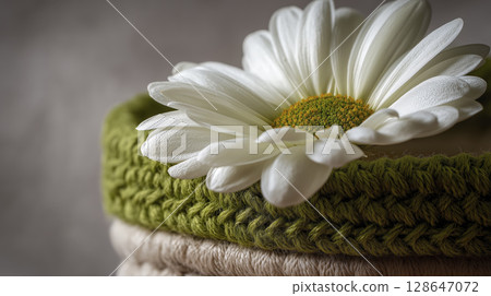 Close up of white daisy flower resting on green knitted fabric, highlighting delicate petals and vibrant yellow center, creating fresh and natural aesthetic 128647072