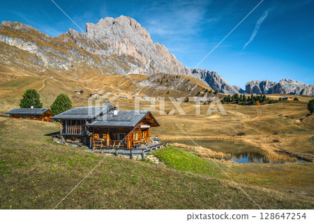 Alpine lake and wooden lodges on the slope, Dolomites, Italy 128647254