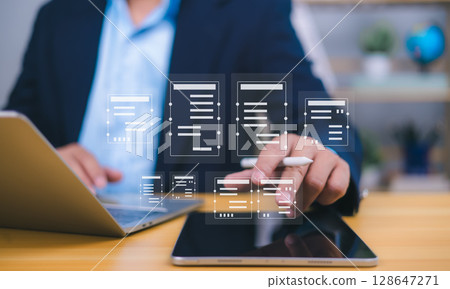Document management visualized by a person interacting with holographic icons from a tablet, with laptop in background, symbolizing digital workflow, remote work, and paperless efficiency. 128647271