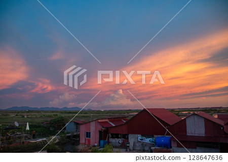 Dramatic sky with vivid sunset colors over tin houses and distant landscape that shows the candid scene of daily life in the rural countryside of Kampot, Cambodia 128647636