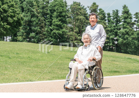 Senior couple (elderly care) walking in a park in a wheelchair Senior couple (elderly care) walking in a park in a wheelchair 128647776