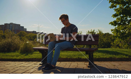 A man reading a book on a park bench 128647912