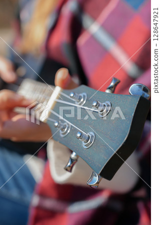 Close up of female hands play ukulele in autumnal park. Young woman plays guitar musical instrument outside in nature fall time. Audio music healing 128647921