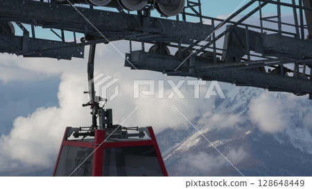 Chairlift Cable Car Mountains Alps Winter Transportation: Scenic Aerial View from Cable Car Cabin above Clouds. Chairlift Cable Car Mountains Alps Winter Transportation: Scenic Aerial View from Cable Car Cabin above Clouds. 128648449