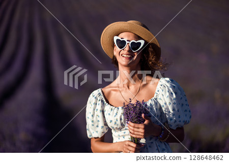 Lavender Woman Sunglasses: Happy woman holds lavender in field during daytime for enjoyment. 128648462