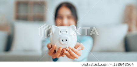 Young Asian woman holding piggy bank and sitting on the floor at home Young Asian woman holding piggy bank and sitting on the floor at home 128648564