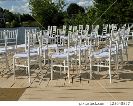 White chairs for the guests of the wedding ceremony are on the site. High quality photo White chairs for the guests of the wedding ceremony are on the site. High quality photo 128648837
