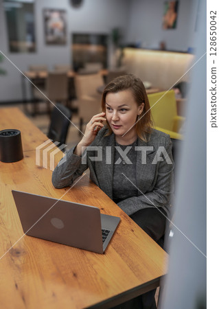 Woman laptop office, woman calls with phone at desk during daytime for business. Woman laptop office, woman calls with phone at desk during daytime for business. 128650042