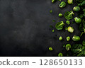 Fresh green Brussels sprouts and leafy vegetables scattered on a dark textured surface, showcasing vibrant colors and natural textures for culinary inspiration and healthy eating 128650133