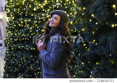 Smiling woman admiring Christmas lights outdoors Smiling woman admiring Christmas lights outdoors 128650721