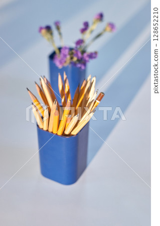 Yellow pencils in blue holders with purple flowers on light surface Yellow pencils in blue holders with purple flowers on light surface 128652210