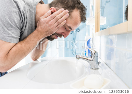 Man washing his face in bathroom Man washing his face in bathroom 128653016