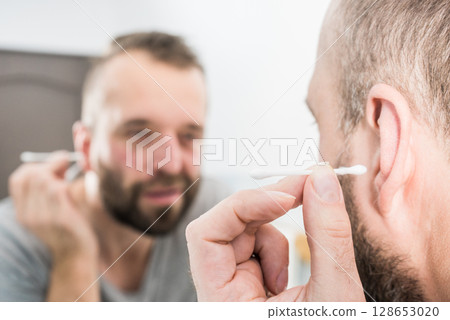 Man removing wax from ear using Q-tip Man removing wax from ear using Q-tip 128653020