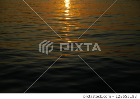 Golden Sunset Reflection on Tranquil Water Surface 128653188