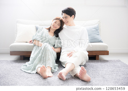 A young couple relaxing in a brightly lit living room. A wide-angle shot of the whole body of a married couple or newlyweds A young couple relaxing in a brightly lit living room. A wide-angle shot of the whole body of a married couple or newlyweds 128653459