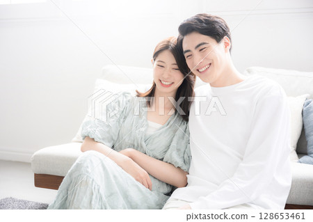 A young couple relaxing in a bright, backlit living room. Image of a married couple or newlyweds 128653461