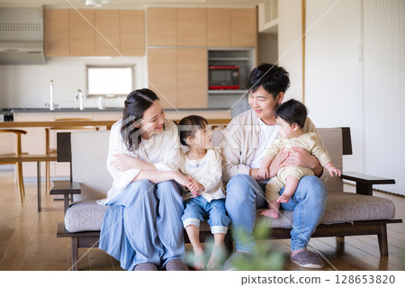 A Japanese family of four relaxing on a sofa in a newly built house with a warm wooden interior 128653820