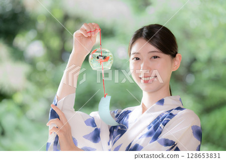 A woman in a yukata holding a wind chime and smiling at the camera 128653831