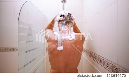 Man washing hair with shampoo in shower, back view Man washing hair with shampoo in shower, back view 128654670