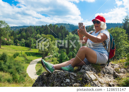 Smiling senior woman taking a selfie while hiking in the mountains Smiling senior woman taking a selfie while hiking in the mountains 128655147
