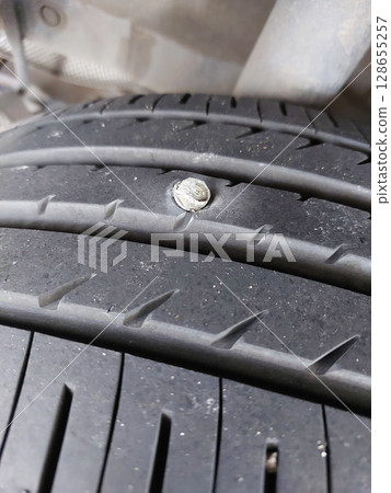 screw puncturing car tire. macro closeup. screw puncturing car tire. macro closeup. 128655257