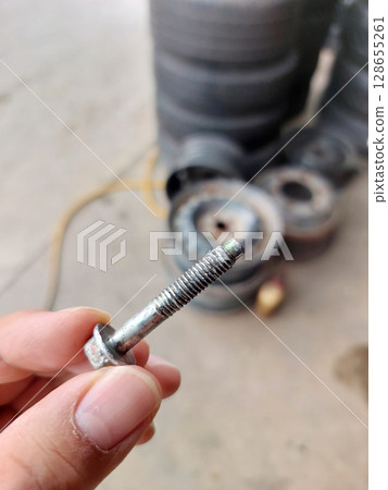 Broken wheel attachment screw. Screw in hand, Car breakdown. Broken wheel attachment screw. Screw in hand, Car breakdown. 128655261