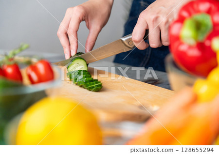 Hands, cutting board and salad in kitchen with green vegetables for healthy eating. Person with cooking skills to prepare lunch with salad, cucumber and organic ingredients at home Hands, cutting board and salad in kitchen with green vegetables for healthy eating. Person with cooking skills to prepare lunch with salad, cucumber and organic ingredients at home 128655294