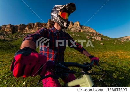 Sports. A cyclist stands alone in a field. A person riding a bicycle in a downhill style. Sports. A cyclist stands alone in a field. A person riding a bicycle in a downhill style. 128655295